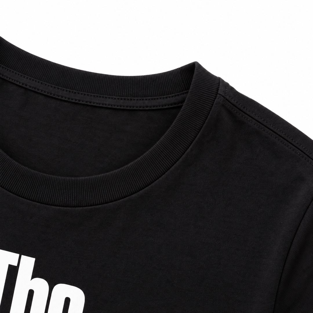 Close-up of a black T-shirt crew neckline and shoulder seam, with the edge of the white printed graphic visible in the frame.