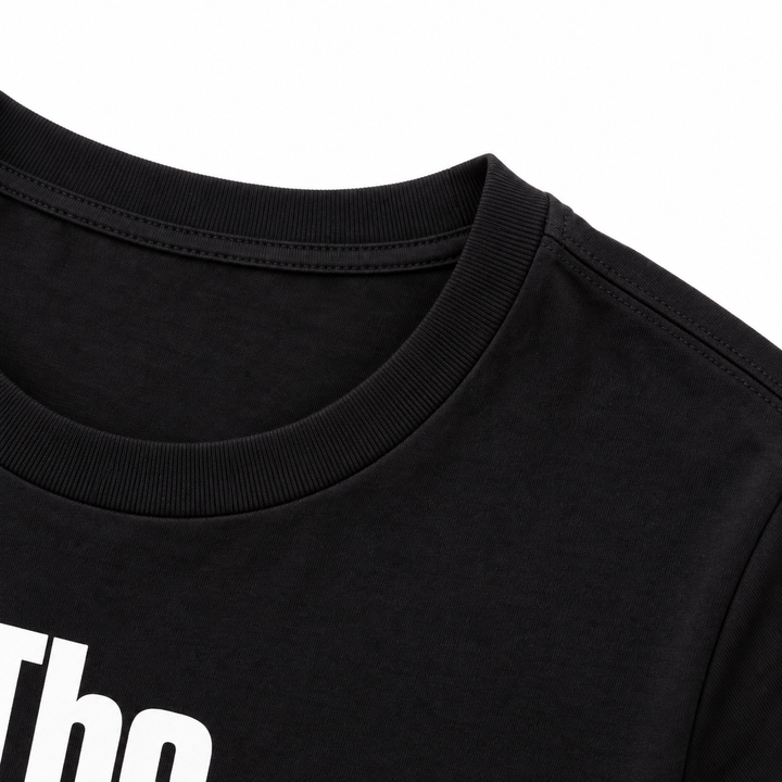 Close-up of a black T-shirt crew neckline and shoulder seam, with the edge of the white printed graphic visible in the frame.