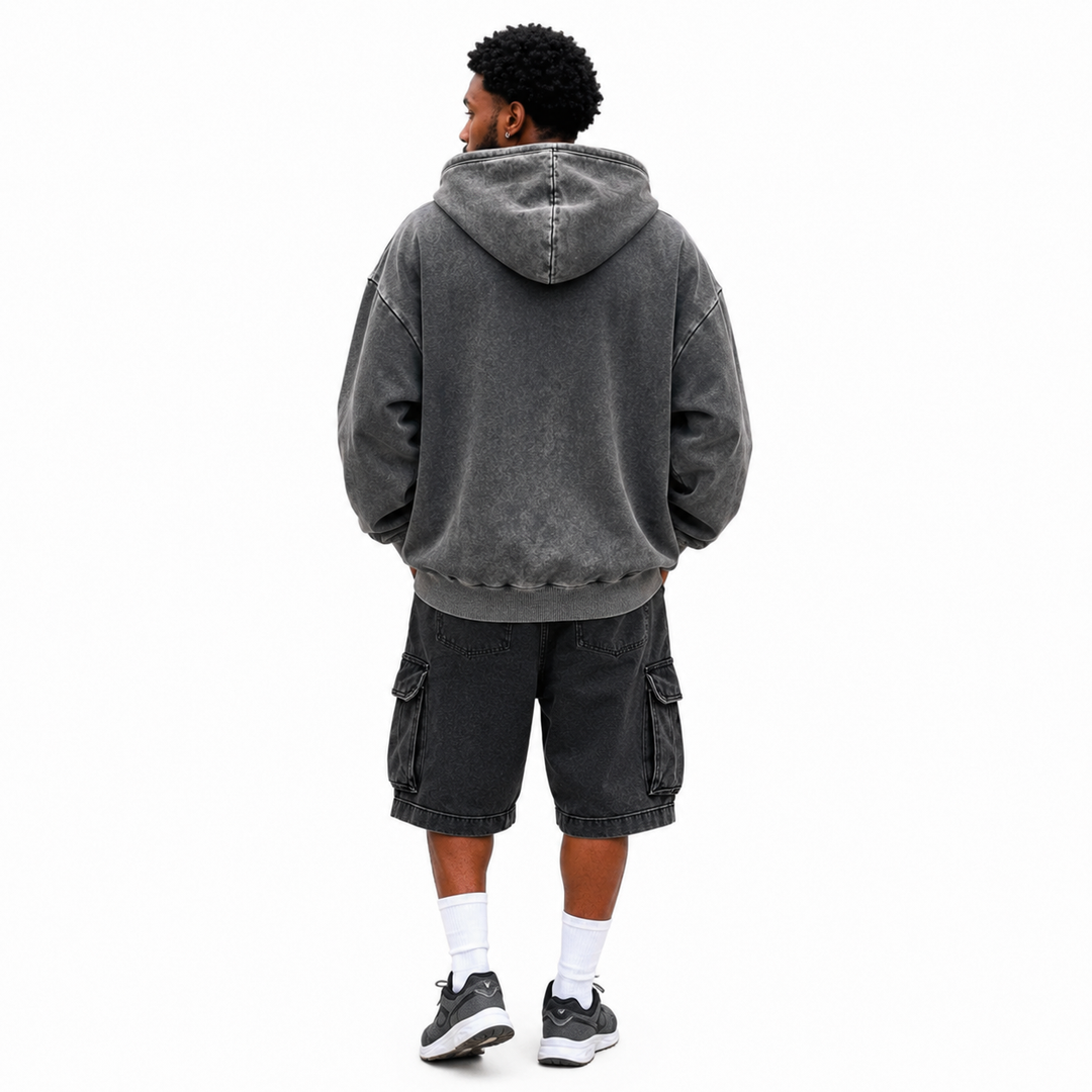 Back view of washed charcoal hoodie on male model showing hood, loose shape, dropped shoulders and ribbed lower hem on white.