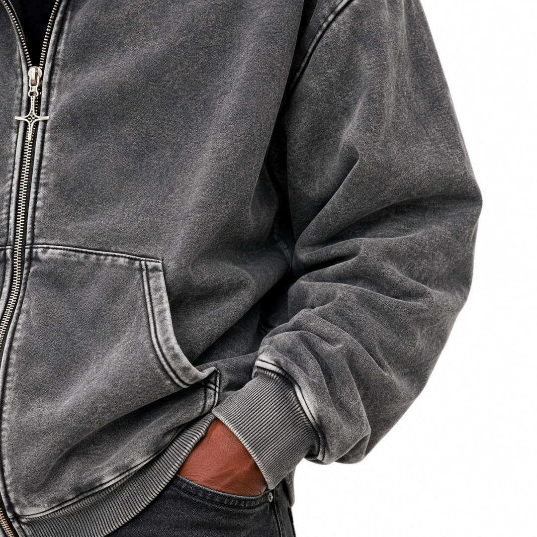 Close view of washed charcoal hoodie fabric showing 65% cotton and 35% polyester texture, stitching and ribbed cuff on white.