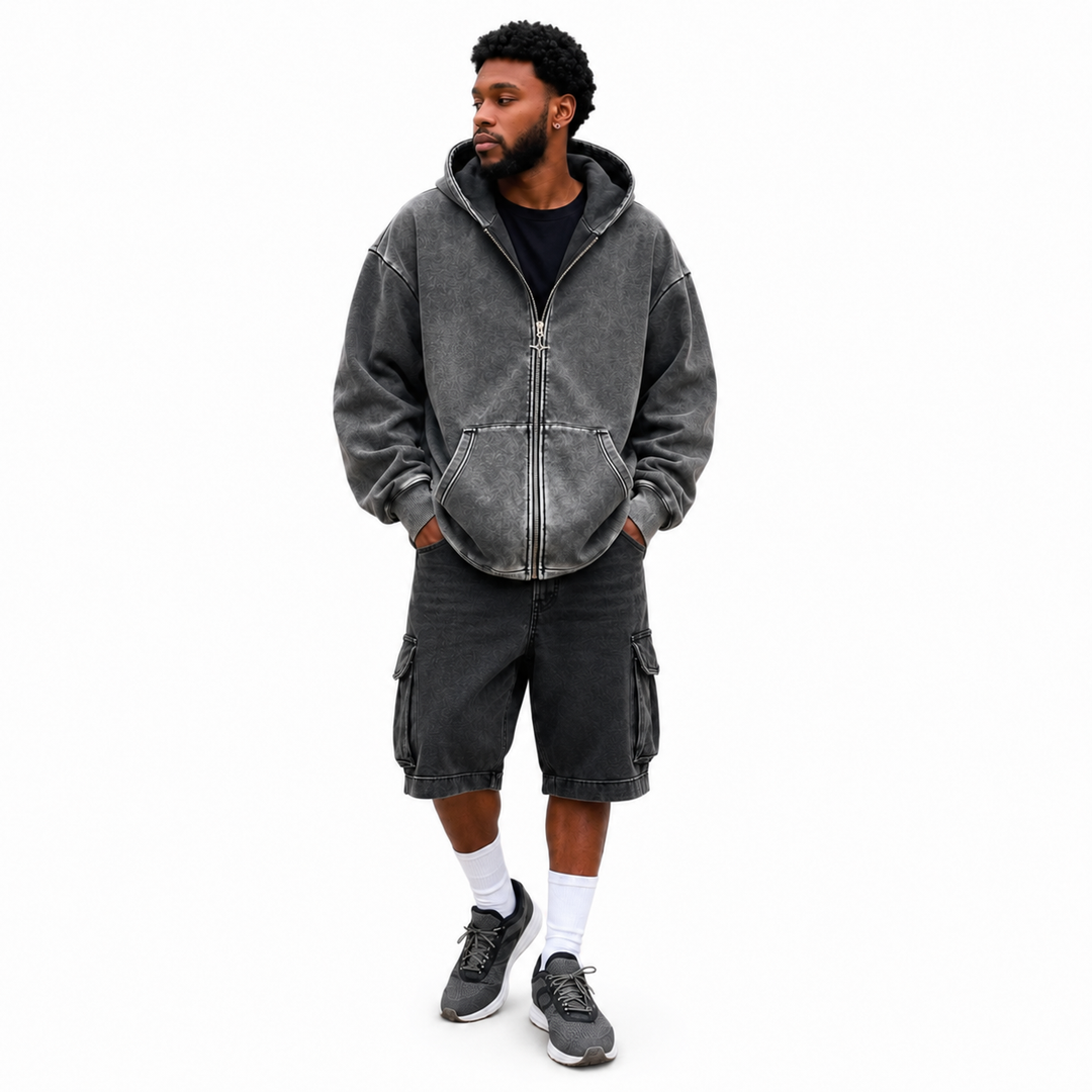 Male model wearing a washed charcoal hoodie with dropped shoulders, relaxed sleeves, front pockets and ribbed cuffs on white.