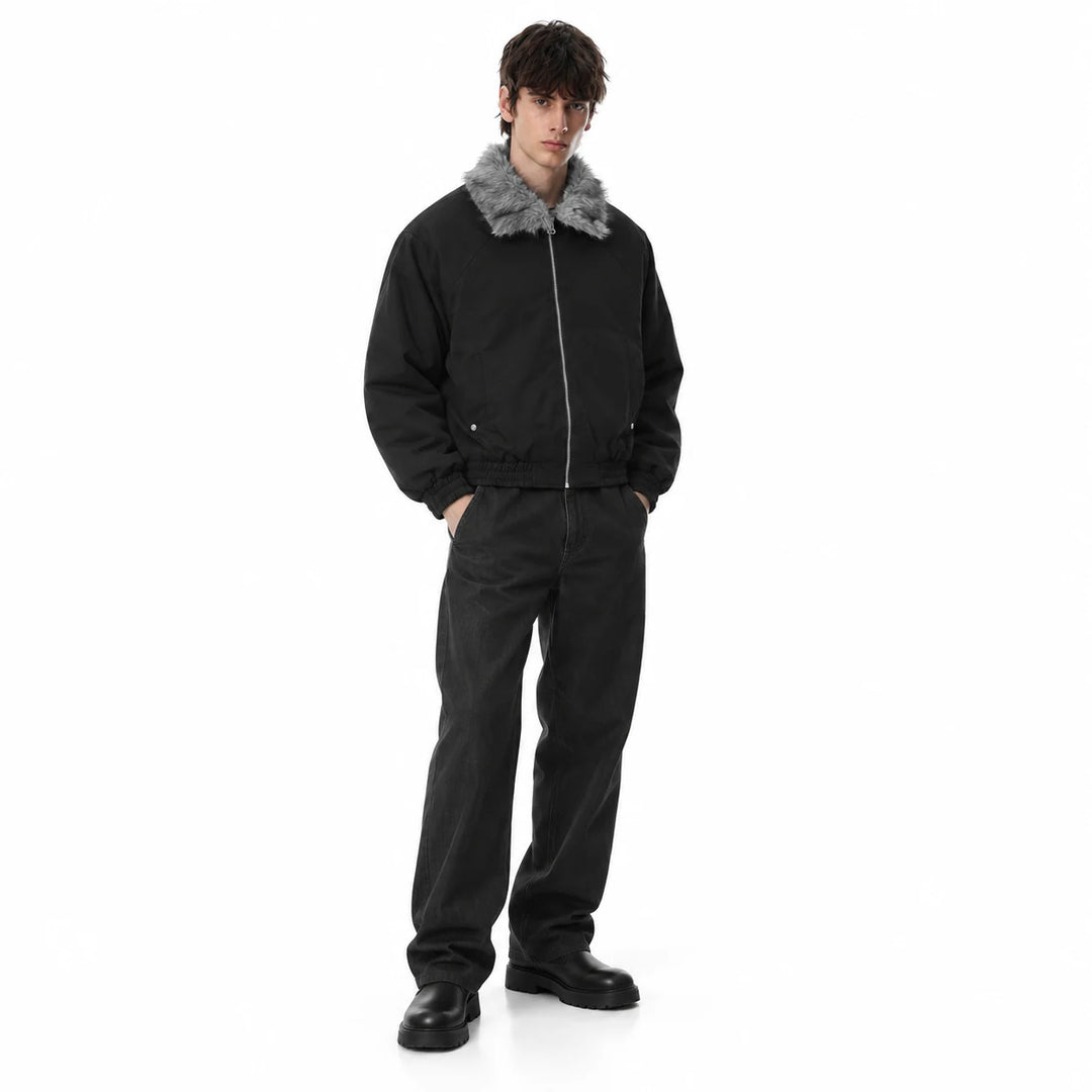 Male model wearing a black padded bomber jacket with grey faux fur collar, wide-leg trousers and boots on a white background.