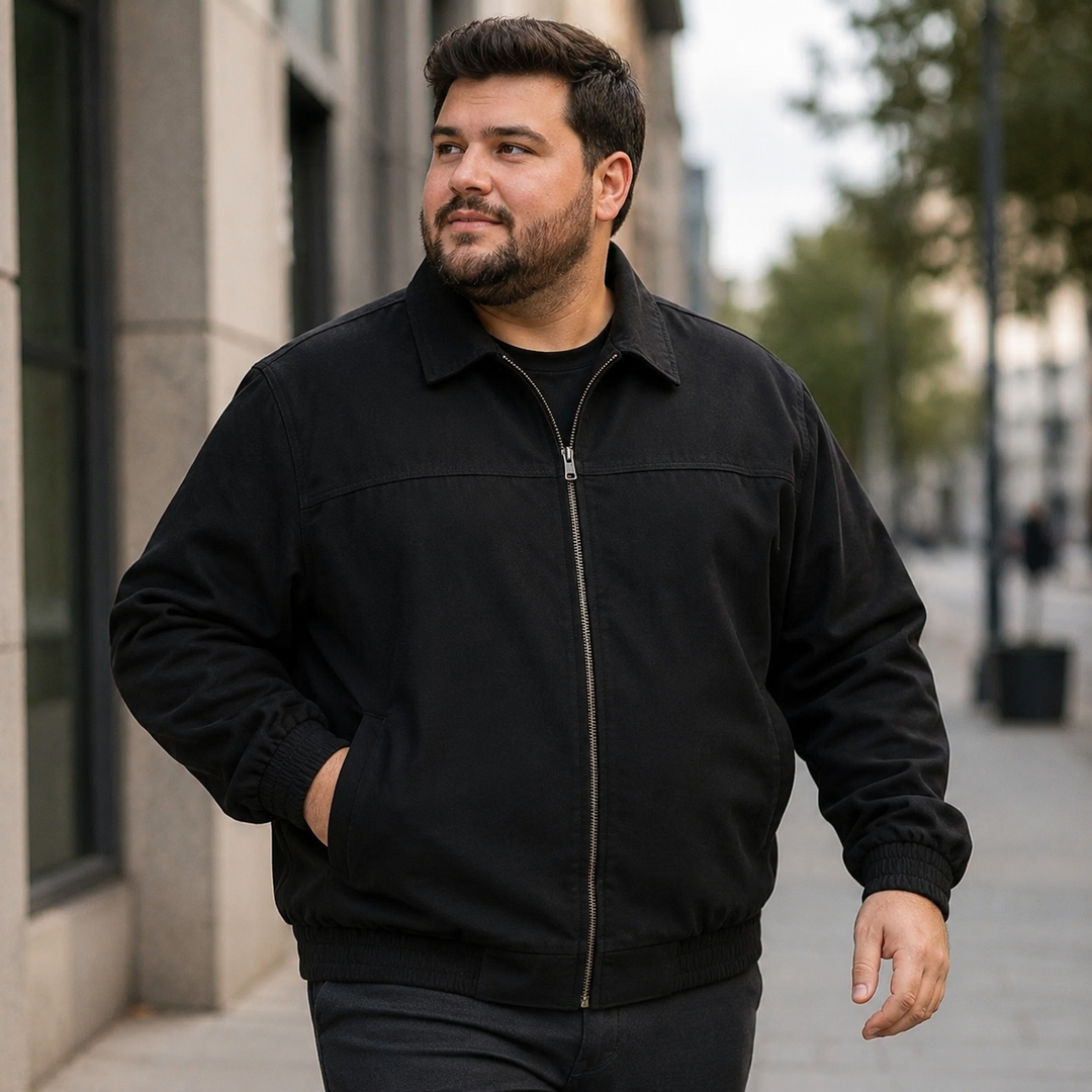 A plus-size male model wearing a black zip-up jacket on a city walkway, showing the fold-down collar and everyday silhouette.