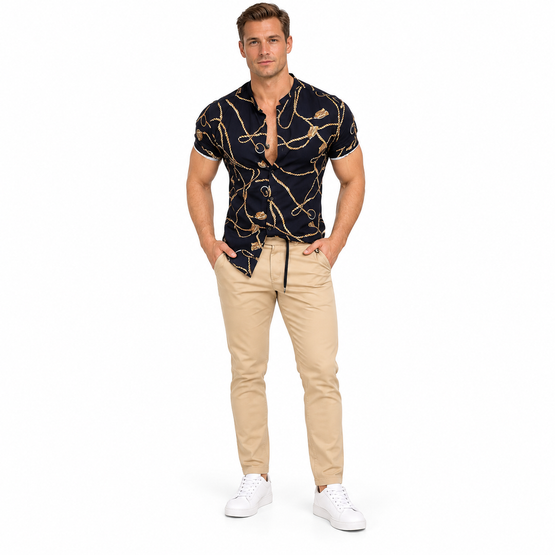 Second male model wearing the black gold chain print collared shirt with beige trousers and white sneakers on white backdrop.