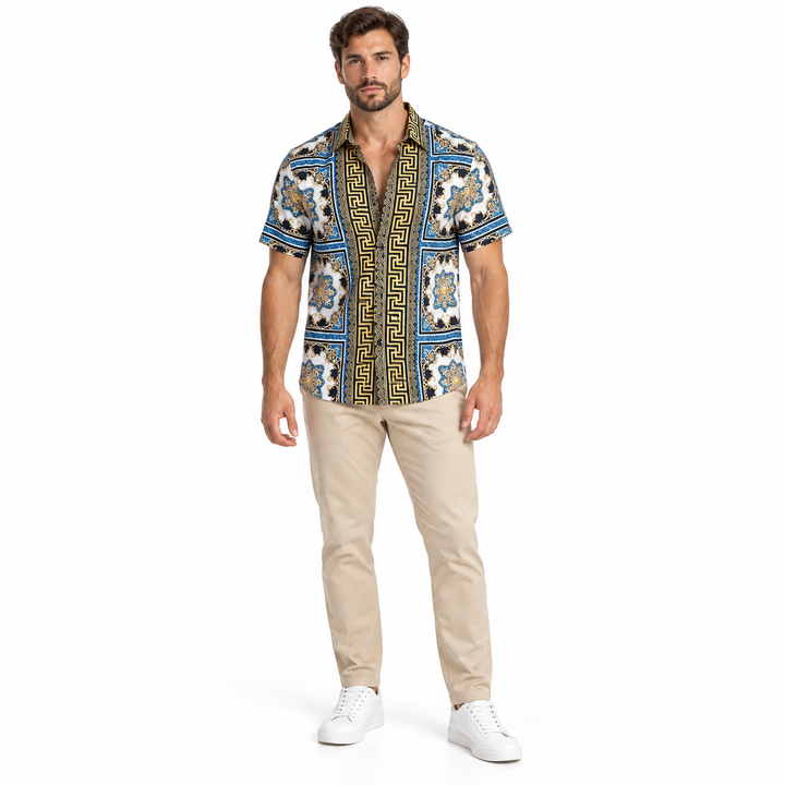 Male model wearing the blue white and gold ornamental short sleeve shirt in beige trousers and white shoes in a white studio.