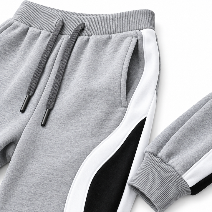 Close-up of Grey jogger pants showing the drawstring waist, pocket, curved side panel, stitching and ribbed cuff.