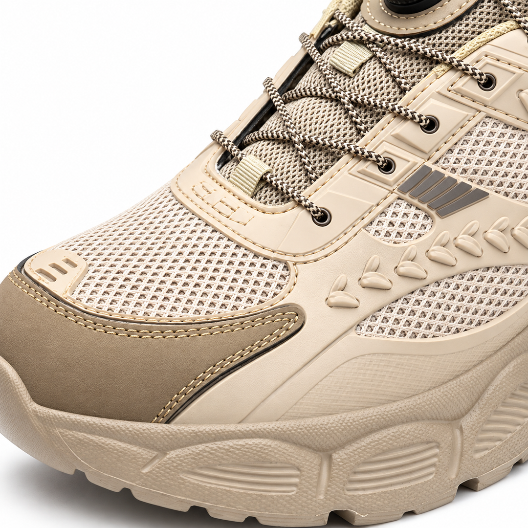 Close-up of beige shoe upper showing mesh texture, stitched toe overlay, cable routing and raised side details in the studio.