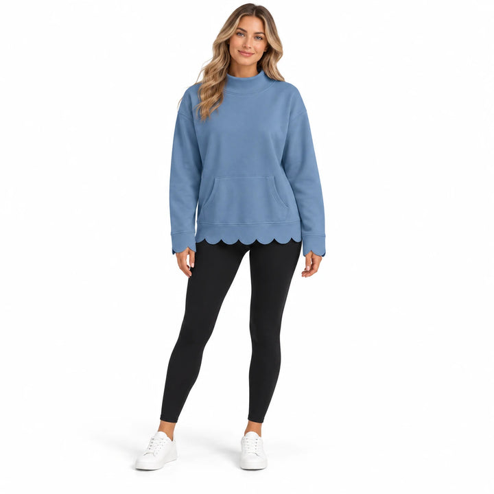 Full-body model in the dusty blue pullover with long sleeves, a center kangaroo pocket and scalloped cuffs and hem, on white.