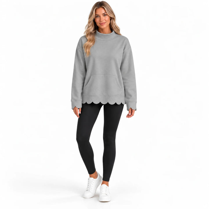 Full-body model in a soft gray pullover with long sleeves, a front kangaroo pocket and scalloped cuffs and hem, on pure white