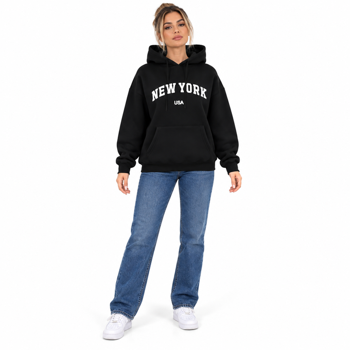 Full body model in a black hoodie with New York USA graphic print, blue jeans and white sneakers on a plain white background.