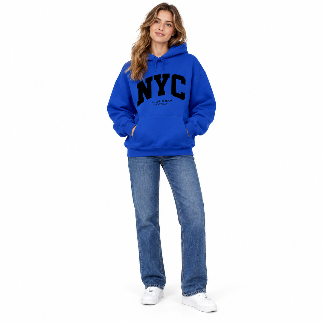 Full body model in a royal blue hoodie with NYC chest print, blue jeans and white sneakers against a white studio background.