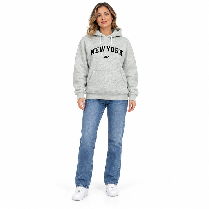 Full body model in a heather gray hoodie with New York USA lettering, blue jeans and white sneakers against a white backdrop.