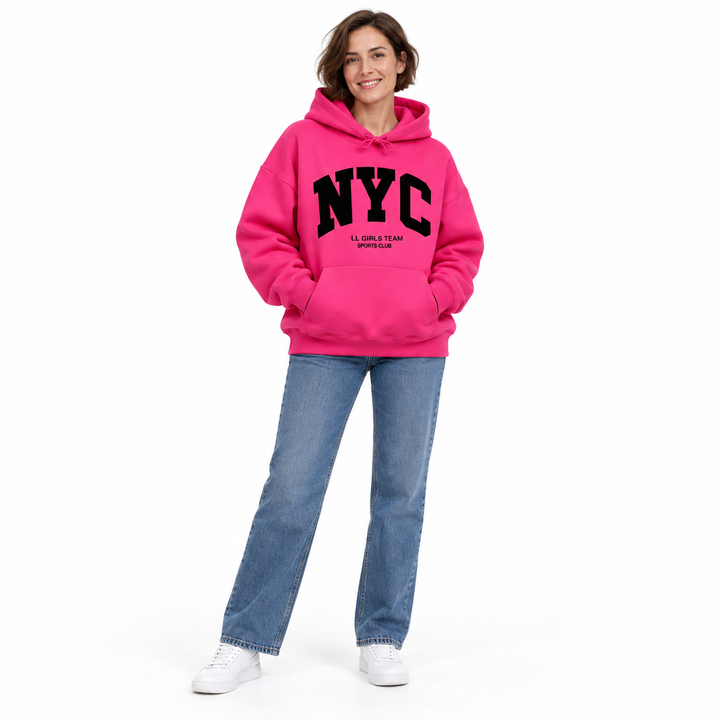 Full body model in a fuchsia hoodie with NYC chest print, long sleeves, jeans and sneakers against a white studio background.