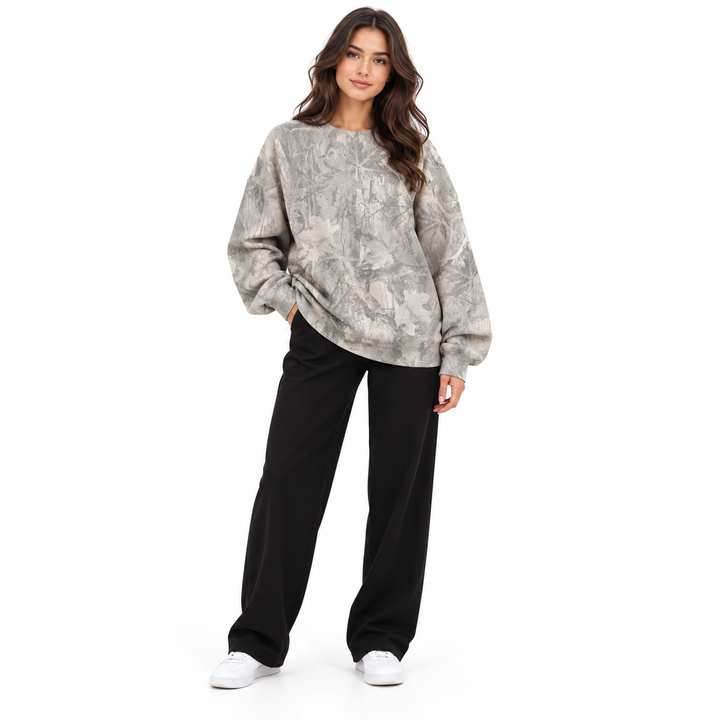 Woman wearing an oversized printed sweatshirt in grey, with a crew neck and long sleeves, standing against a white background