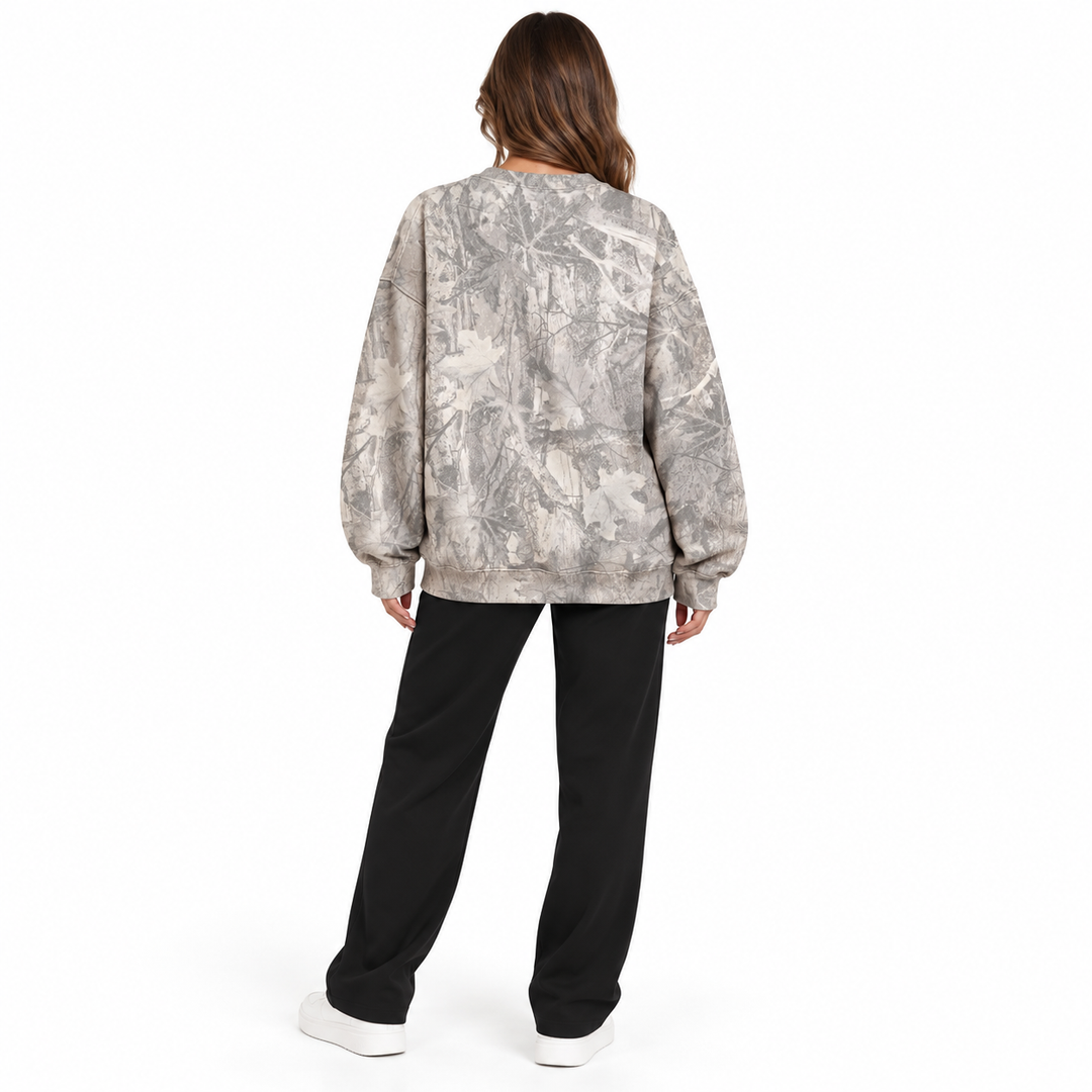 Woman in a grey branch print sweatshirt viewed from behind with the back print and sleeves visible in a white studio setting.