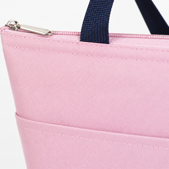 Pink Oxford cloth lunch tote close-up showing woven texture, precise stitching, metal zipper pull and dark navy handle detail