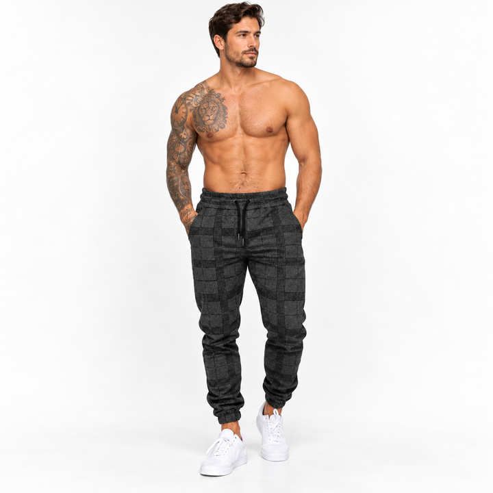 Dark grey plaid jogger pants on male model in clean studio hero view, showing tapered silhouette, drawstring and ankle cuffs.