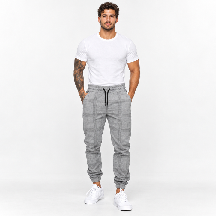 Plaid pants for men in light grey on male model, front studio view with check pattern, black drawstring and tapered leg cuffs