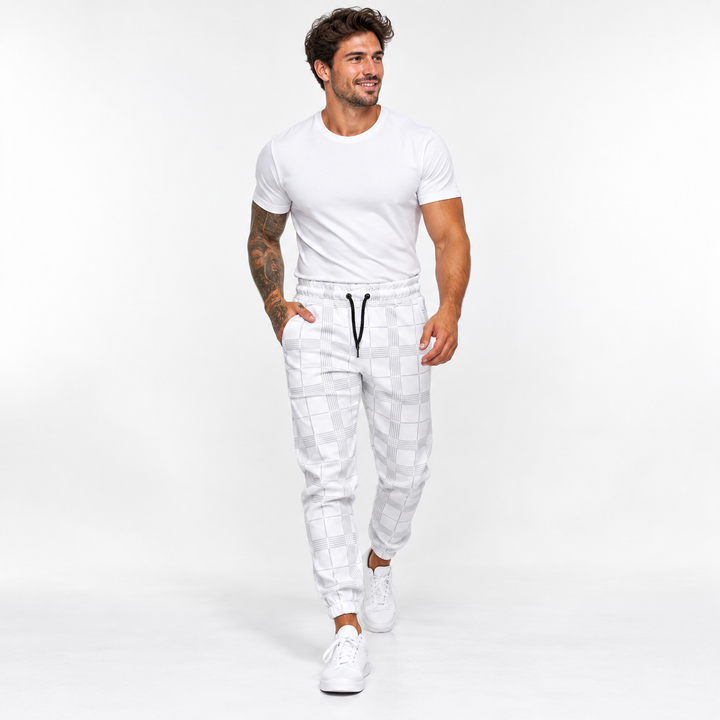 Plaid pants for men in white on male model walking in studio, showing tapered jogger shape, black drawstring and ankle cuffs.