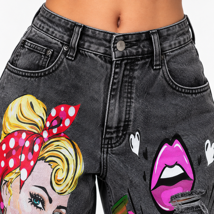 Close-up of dark blue denim with colorful illustrated art print, distressed edges and visible washed texture.