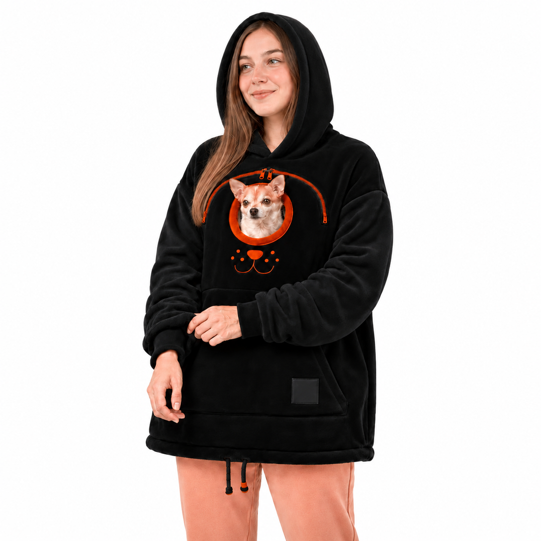Woman wearing a black fleece lined hoodie with a front pocket, orange zipper and small dog against a white studio background.