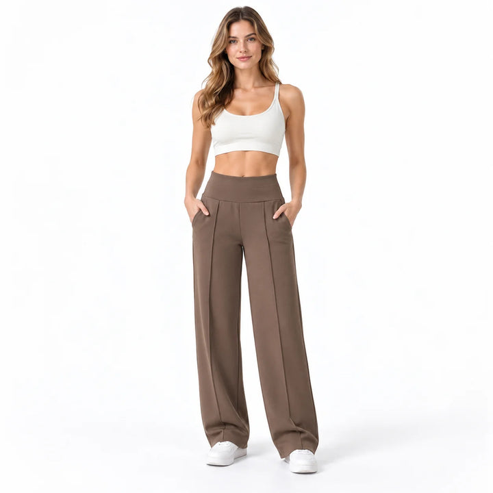 Coffee brown trousers on a full-body female model in a white studio, showing a wide waistband, front pleats and side pockets.