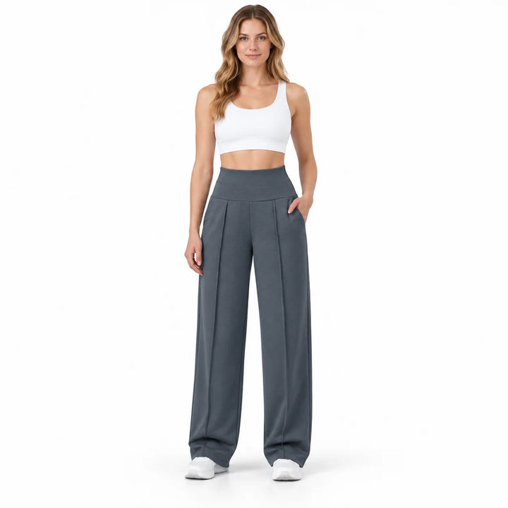 Dark gray pants worn by a full-body model in a white studio, showing the high waistband, curved side pockets and front pleats