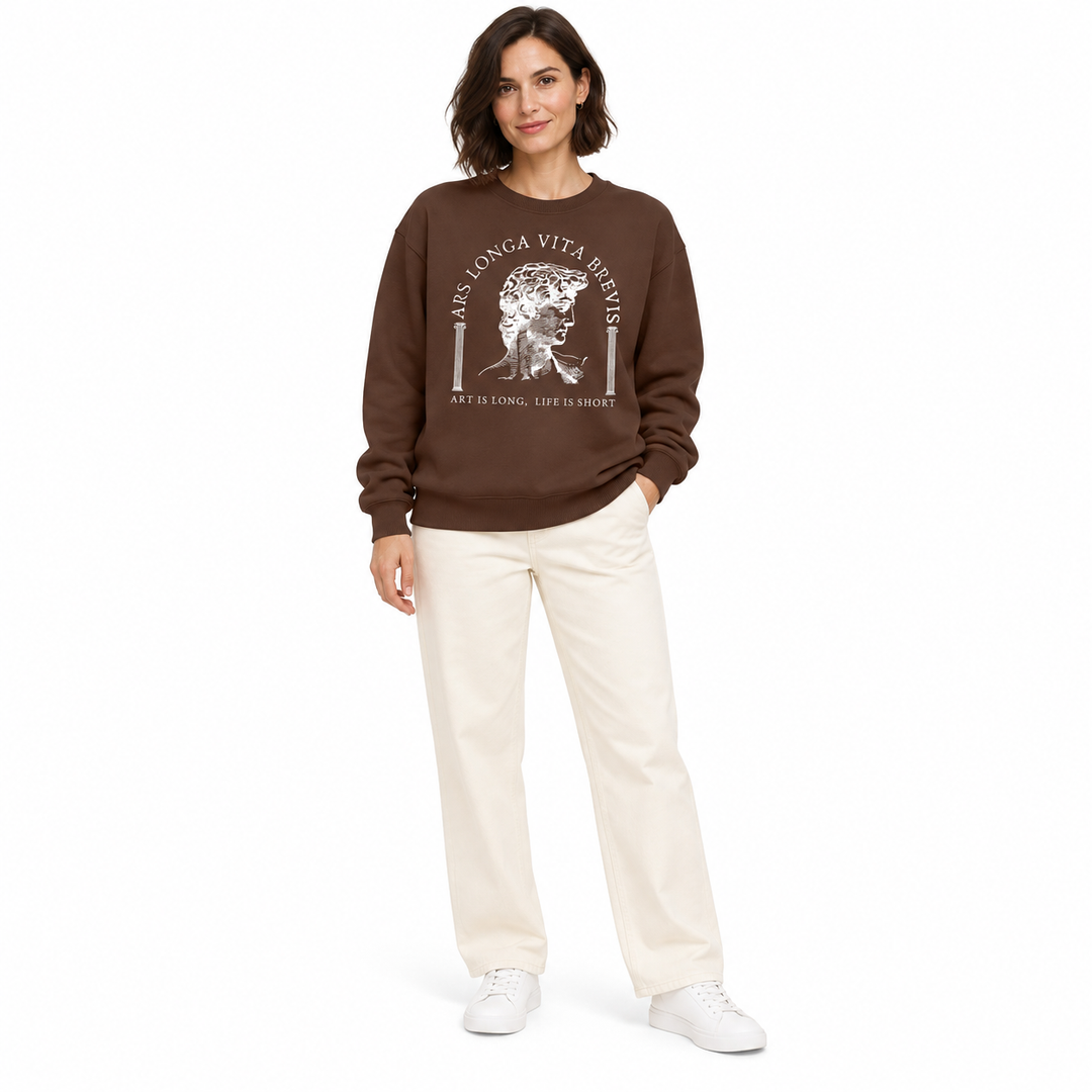 Coffee brown sweatshirt with white sculpture print on a second full-length woman, styled with ivory trousers and white shoes.
