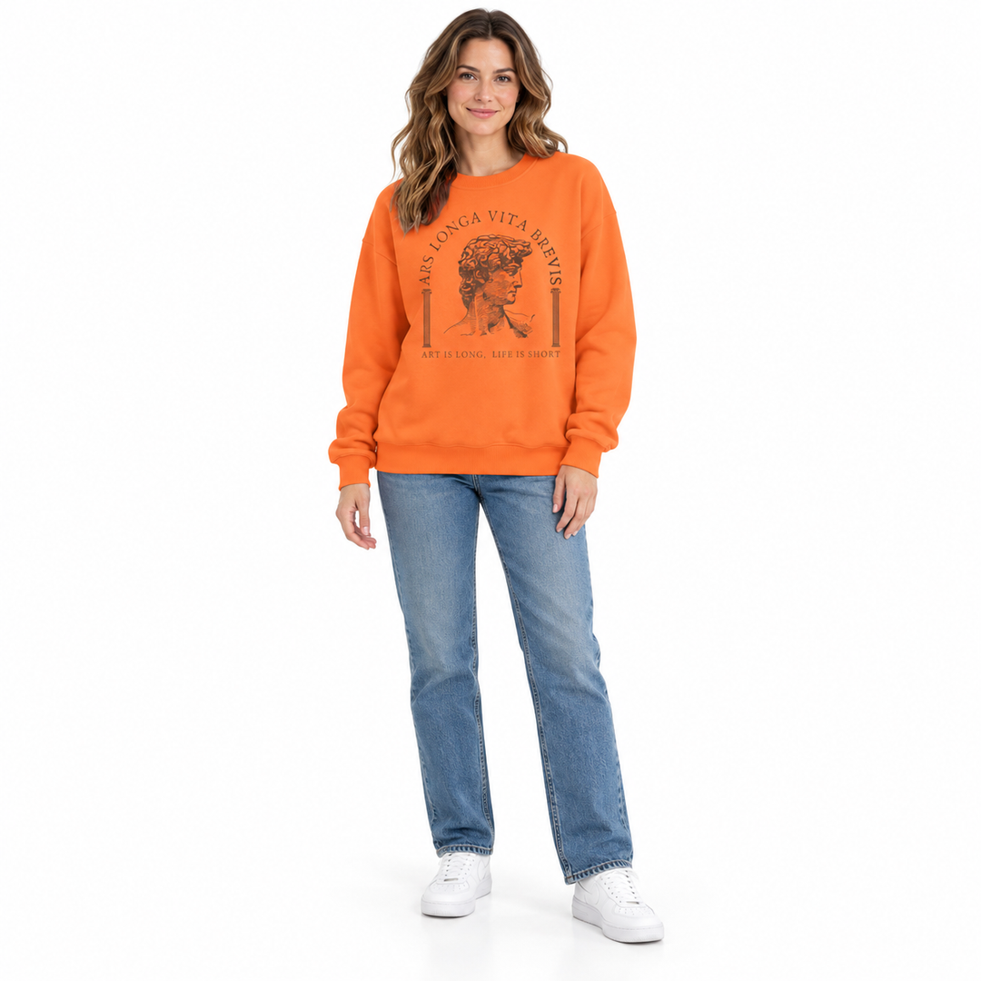 Orange sweatshirt on a full-length woman with brown sculpture print, dropped shoulders, blue jeans and white shoes in studio.