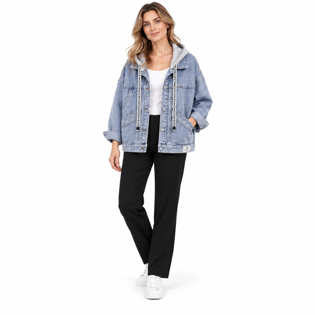 Women's denim jacket worn by a model, showing washed blue denim, grey hood, curved front pockets, and a relaxed studio stance