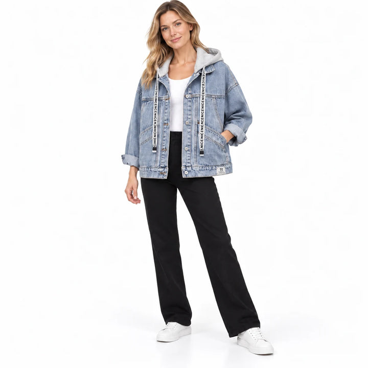Full front view of the washed blue jacket with grey hood on an adult model, with black trousers and plain white studio shoes.