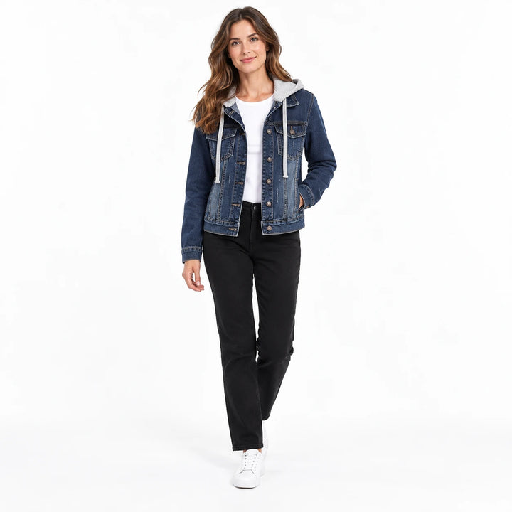 Model walking in a dark blue denim jacket with a grey hood and drawstrings, black trousers and white shoes in a white studio.