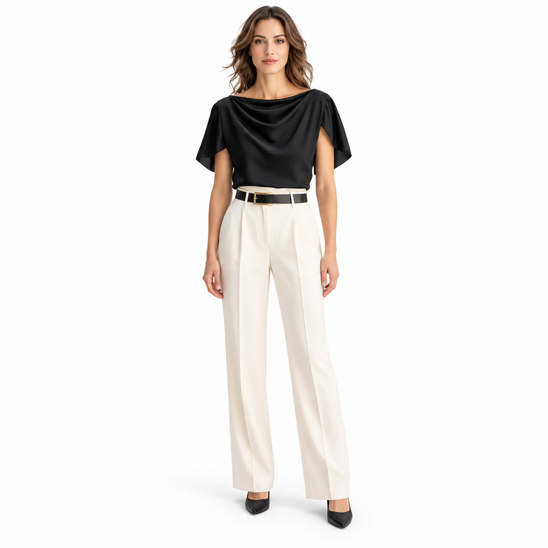 Front view of model in a black blouse with draped neckline and short sleeves, ivory trousers and heels on a white background.