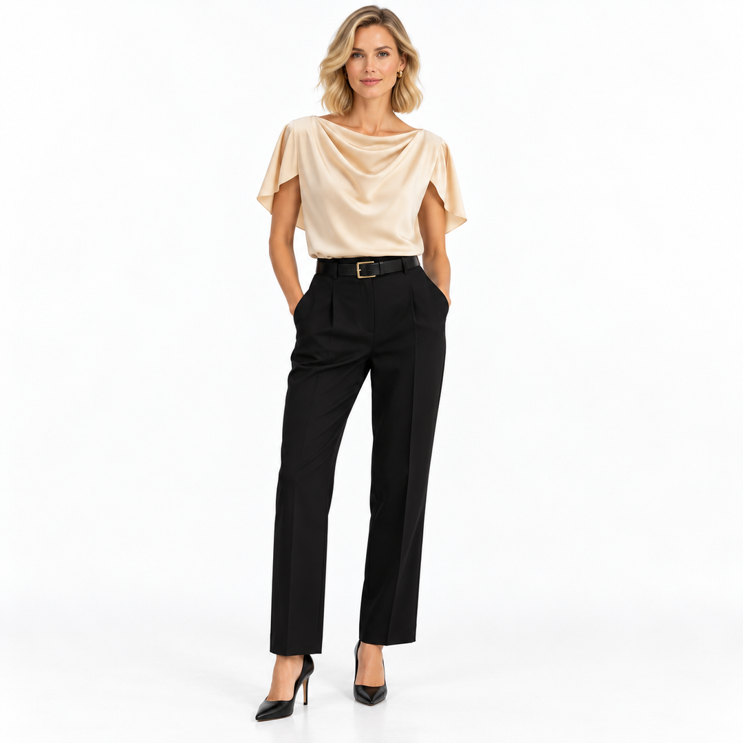Blonde model wearing an apricot blouse with flutter sleeves, black trousers and heels, shown full length on white background.