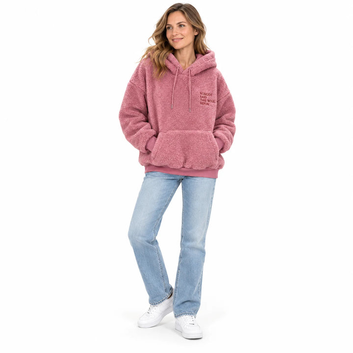 Pink fleece pullover worn by an adult woman, showing the drawstring hood and front pocket, against a white studio background.