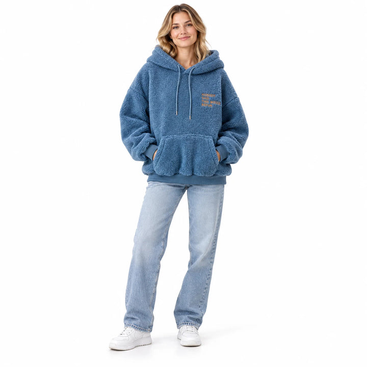 Blue fleece pullover worn by an adult woman, showing the drawstring hood and front pocket, against a white studio background.