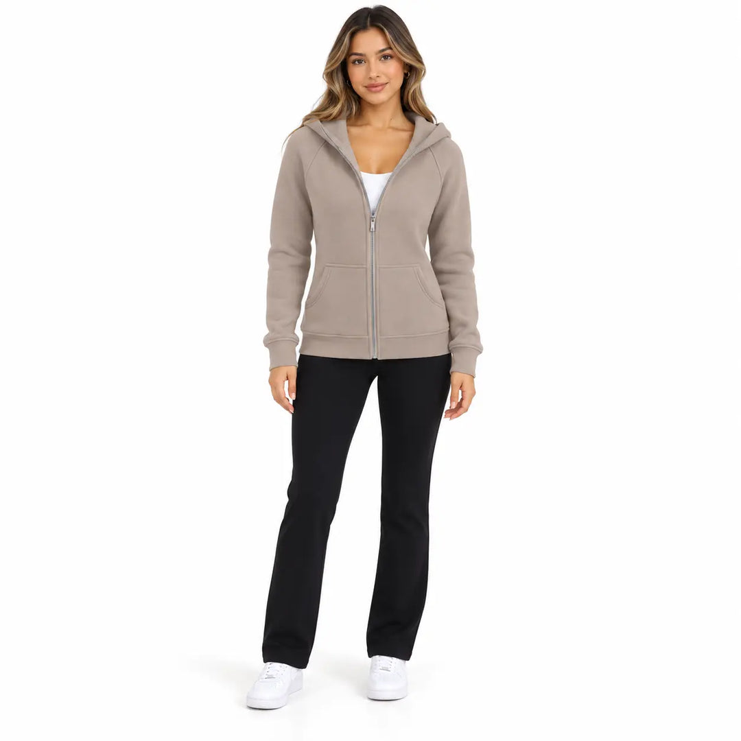 Full-body model wearing the Warm Taupe zip hoodie, showing front pockets, ribbed cuffs and hem, on white with black trousers.