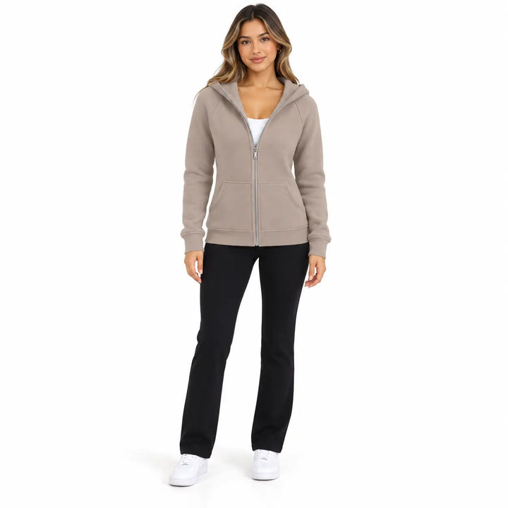 Full-body model wearing the Warm Taupe zip hoodie, showing front pockets, ribbed cuffs and hem, on white with black trousers.