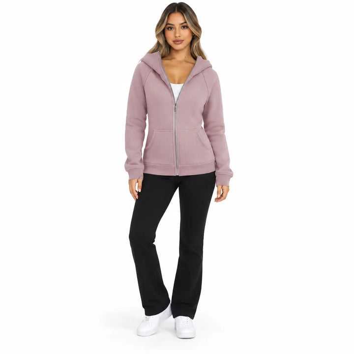Full-body model wearing the Dusty Rose zip hoodie, showing front pockets, ribbed cuffs and hem, on white with black trousers.