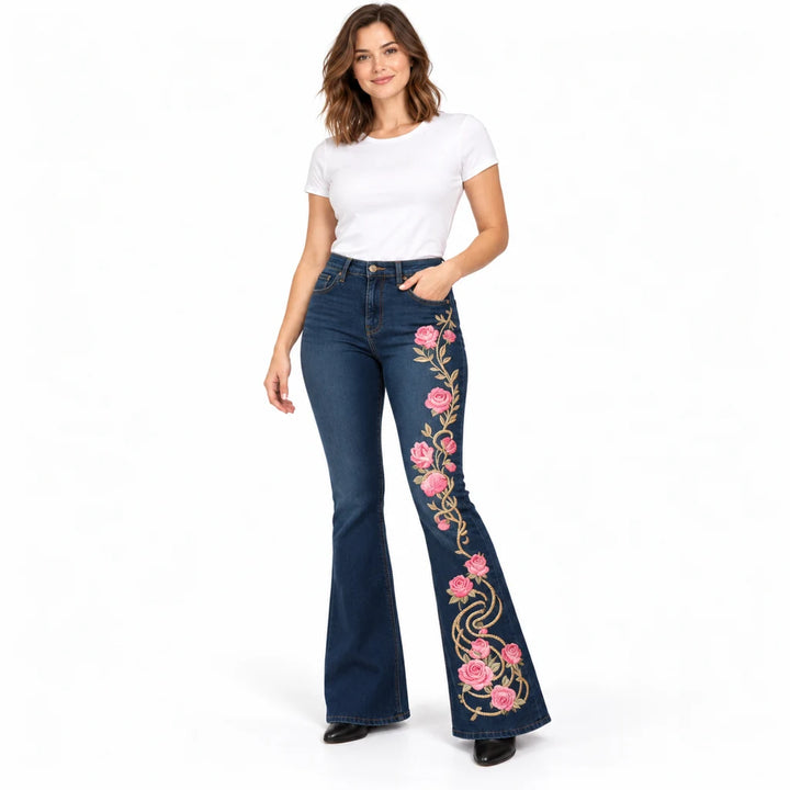 Model wearing dark blue floral flare jeans with pink roses, gold-tone vine print and slim-fit upper legs on white background.