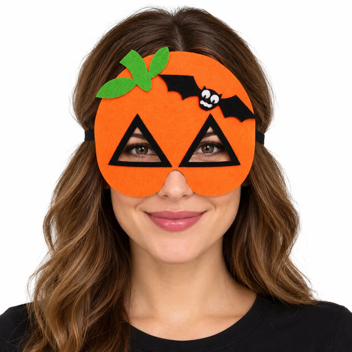 Adult woman wearing an orange pumpkin felt mask with triangular eye openings, green leaves and black bat on white background.