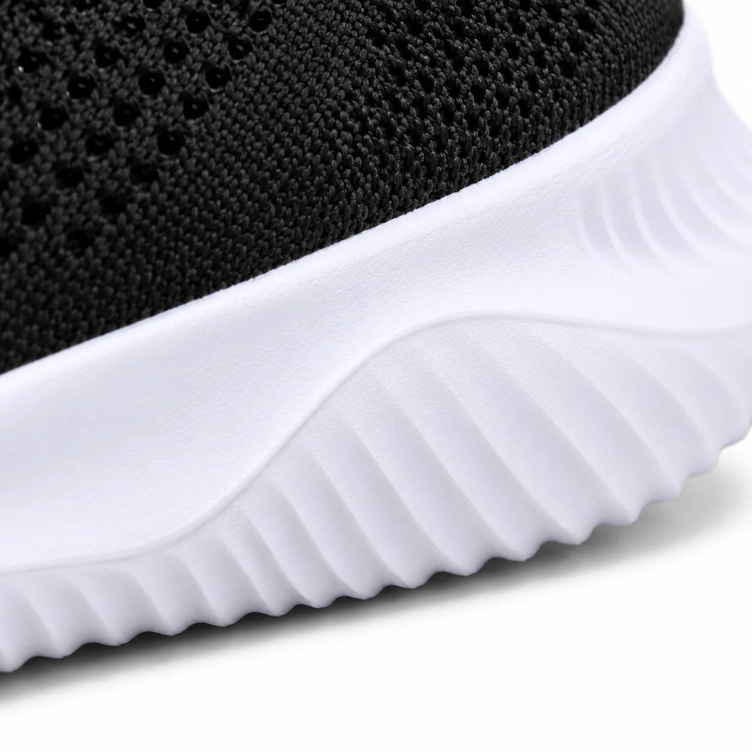 Close side view of the white sneaker sole with diagonal sculpted ridges and a small band of black knitted mesh along its top.