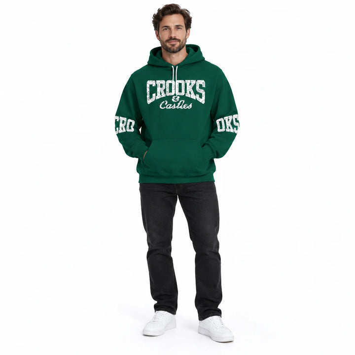 Full-length male model wearing a Forest Green graphic hoodie with chest and sleeve prints on a white studio background