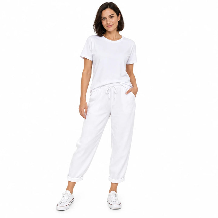 White two-piece outfit worn by an adult woman, with a plain short-sleeve top and drawstring pants, in a white studio setting.
