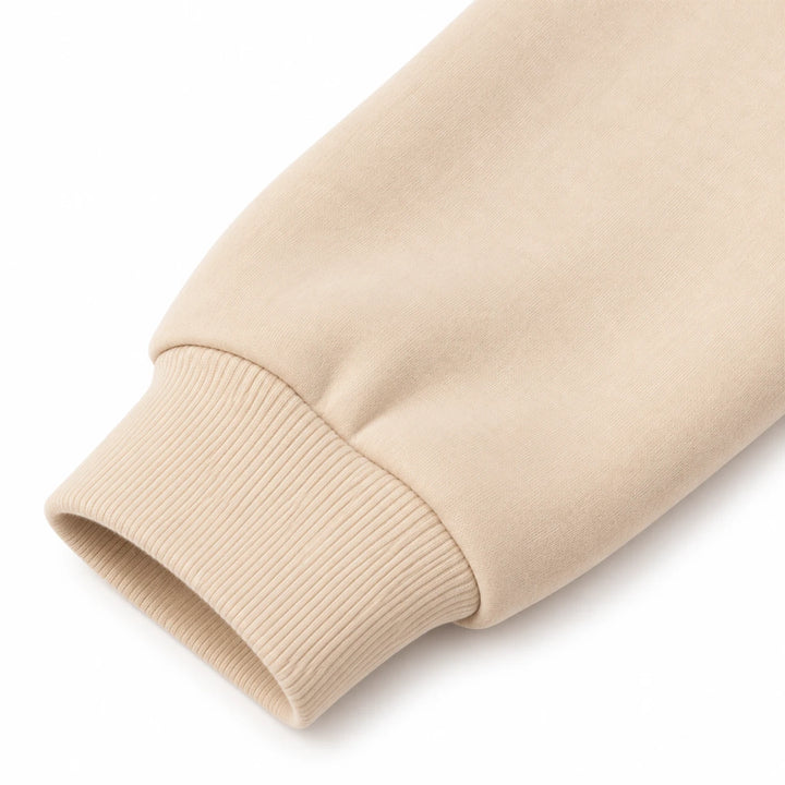 Close-up of the beige pullover fabric and ribbed sleeve cuff, showing visible exterior details, on a seamless white backdrop.