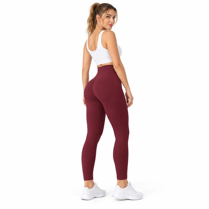 Adult model wearing Plum Wine Red high-waisted leggings in a rear three-quarter view, with a white top and trainers on white.