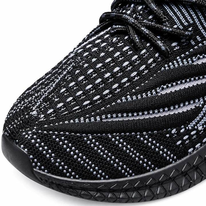 Close view of the black sneaker toe box, showing the knit pattern and pale gray mesh details in a studio photograph on white.