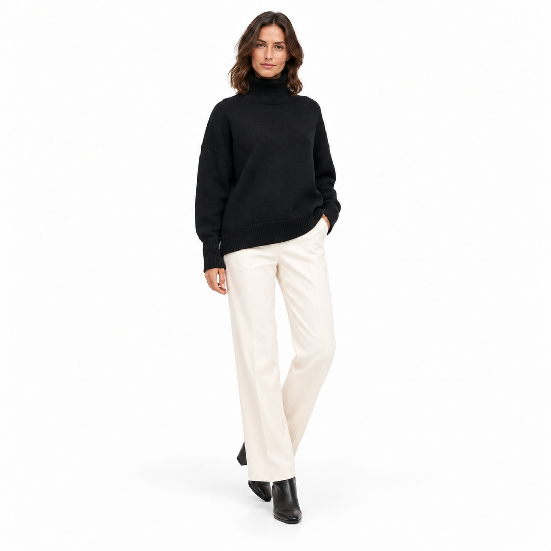 Angled front view of a model wearing the black turtleneck sweater, ivory trousers and ankle boots against a white background.