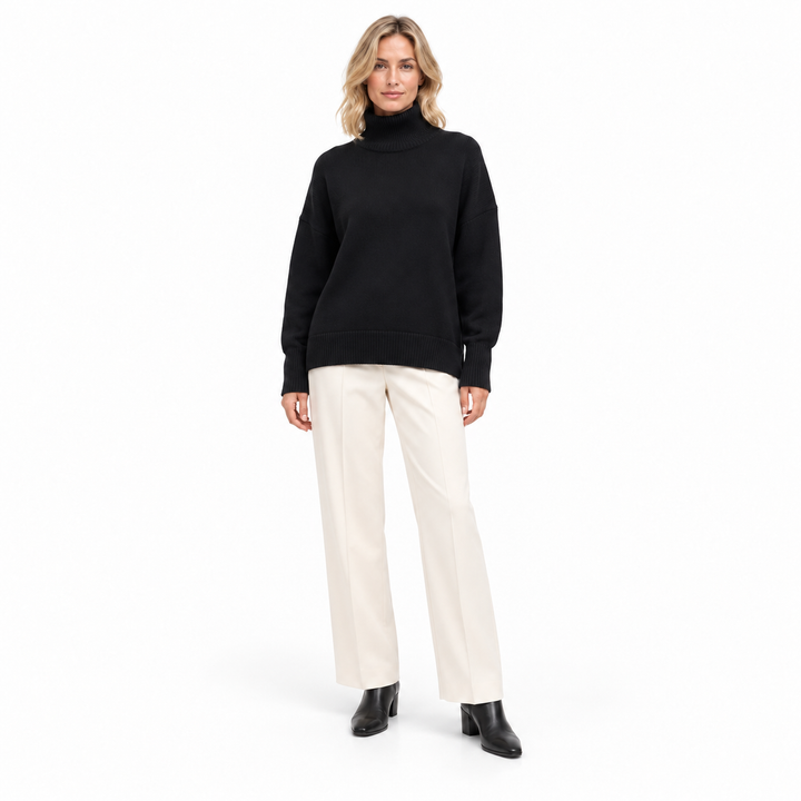 Second adult model with blond hair wearing the black turtleneck sweater with ivory trousers and black boots in a white studio