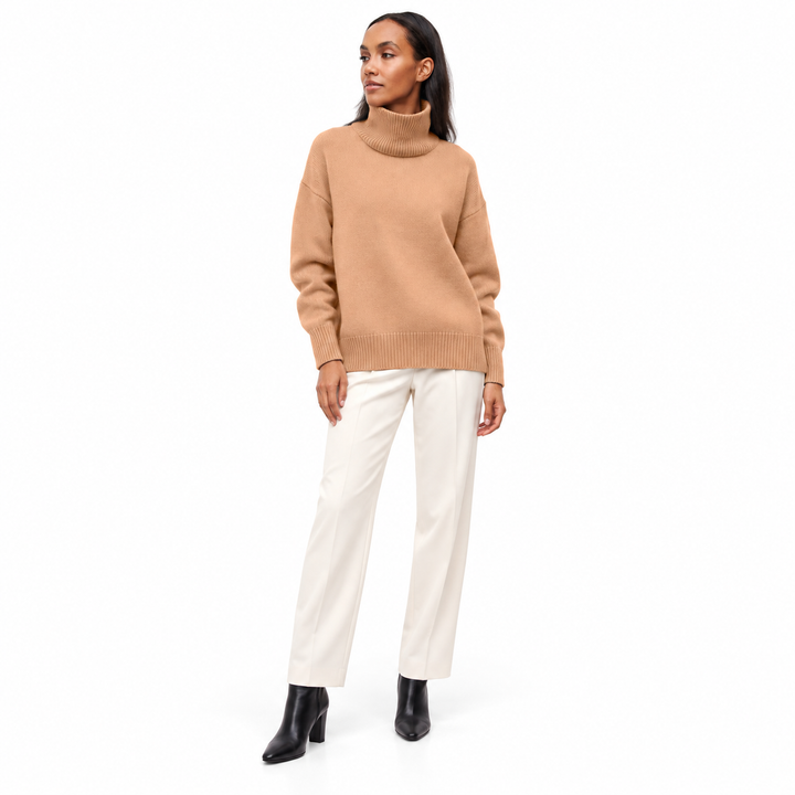 Full-length model wearing a camel turtleneck sweater with ivory tailored trousers and black boots against a white background.